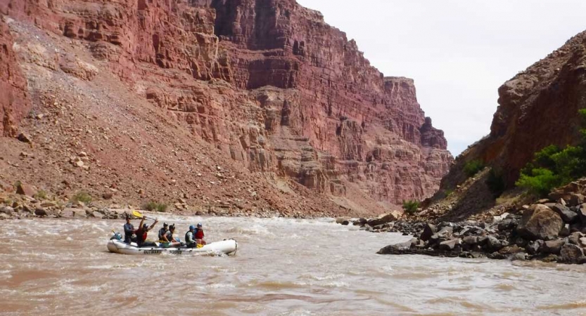 People paddle a raft through whitewater framed by tall canyon walls. 